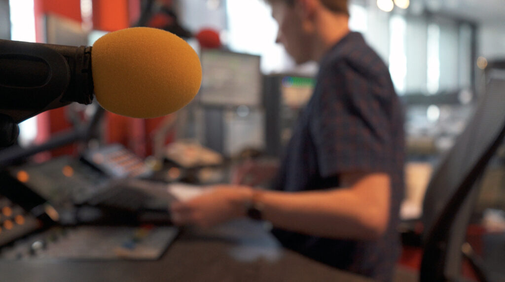 Jamie Moreland sat behind a mixing desk in a BBC radio studio, with a yellow microphone in the foreground